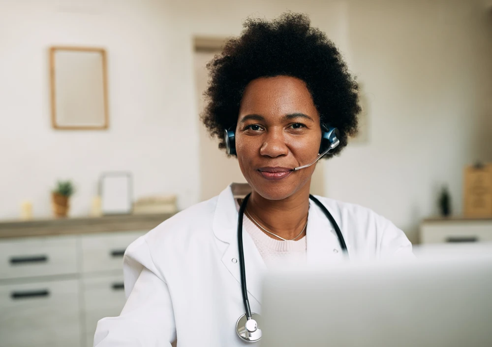 Smiling MaNaDr Ghana doctor wearing a headset and stethoscope, ready to help over a video call